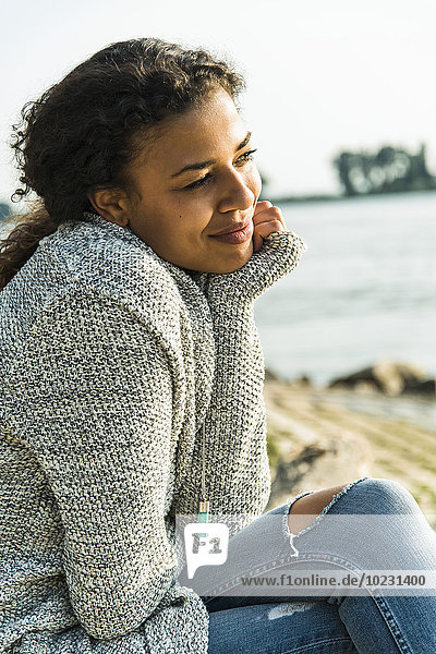 Lächelnde junge Frau sitzt am Flussufer