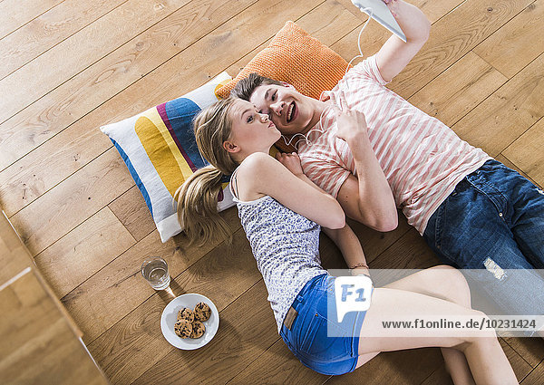 Ein glückliches junges Paar liegt auf dem Boden und teilt sich ein digitales Tablett.