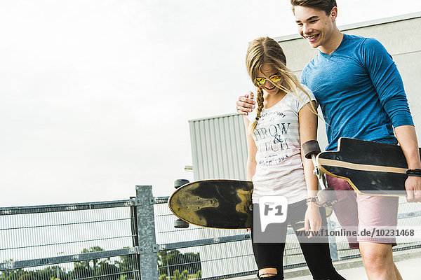 Fröhliches junges Paar  das mit Skateboards läuft.