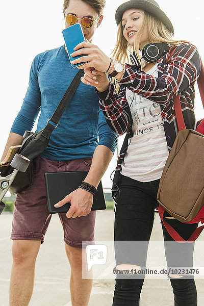 Glückliches junges Paar im Freien mit Skateboard und Handy