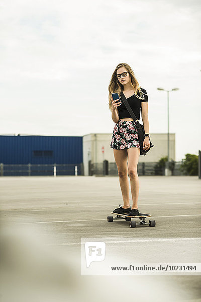 Teenager-Mädchen beim Skateboardfahren auf dem Handy