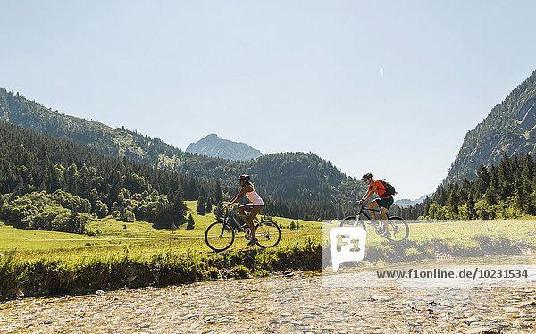 Austria  Tyrol  Tannheim Valley  young couple riding mountain bike at riverside