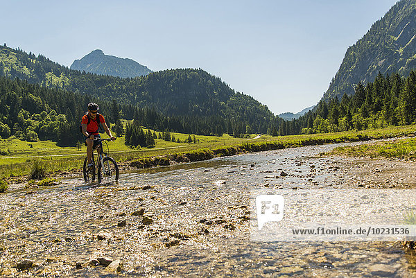 Österreich  Tirol  Tannheimer Tal  junger Mann auf dem Mountainbike überquert Bach