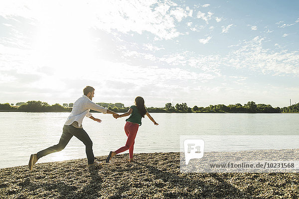 Young couple running hand in hand by the riverside