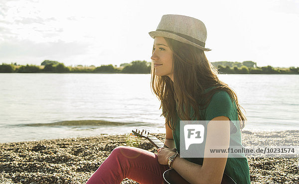 Junge Frau mit Gitarre am Flussufer sitzend