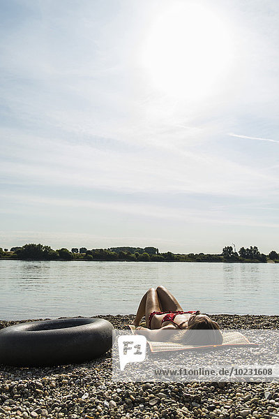 Junge Frau im Bikini beim Sonnenbaden am Flussufer