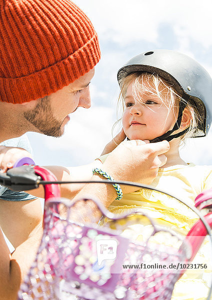 Vater schließt den Helm der Tochter auf dem Fahrrad