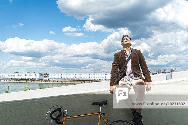 Erwachsener Mann mit Fahrrad auf der Wand sitzend und das Wetter genießend
