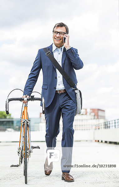 Geschäftsmann schiebt Fahrrad beim Telefonieren