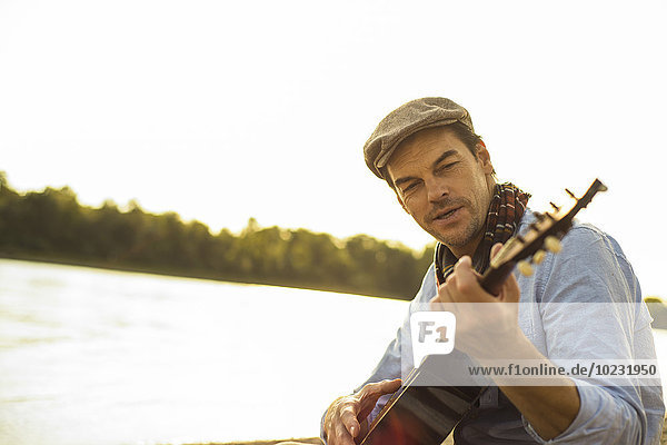 Portrait of man playing guitar at riverside in the evening