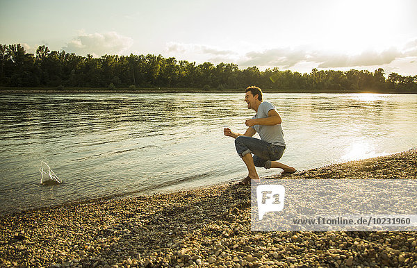 Man crouching at riverside throwing pebbles into the water