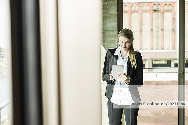 Junge Geschäftsfrau am Fenster mit Blick auf das digitale Tablett