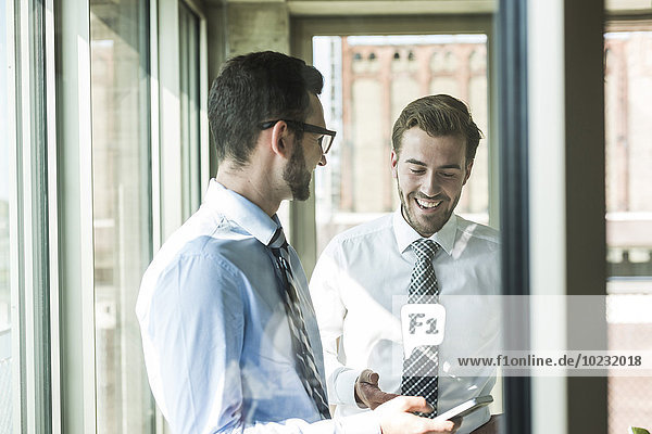 Two happy young businessmen with smartphone at the window