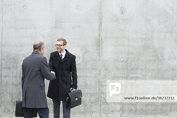 Two businessmen shaking hands at concrete wall