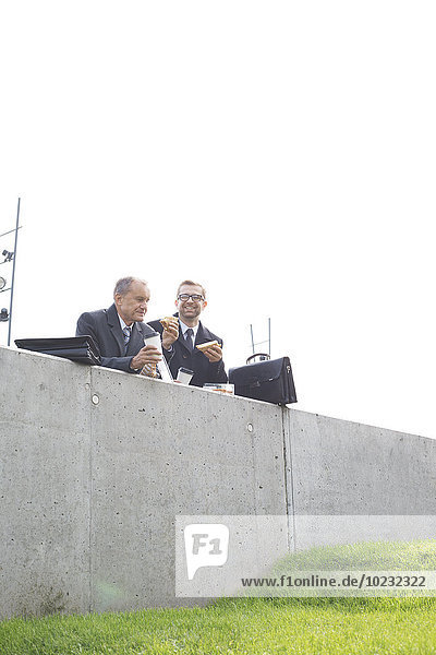 Two businessmen having lunch break at concrete wall