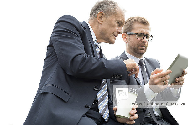 Zwei Geschäftsleute mit digitalem Tablett und Kaffee für unterwegs