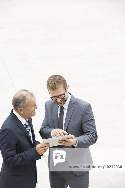 Two businessmen with digital tablet standing on square