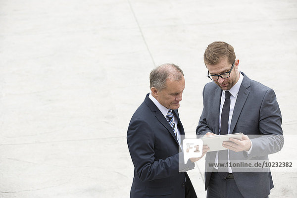 Two businessmen with digital tablet standing on square