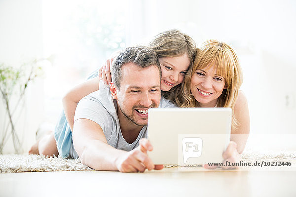 Glückliche Familie auf dem Boden liegend mit digitalem Tablett