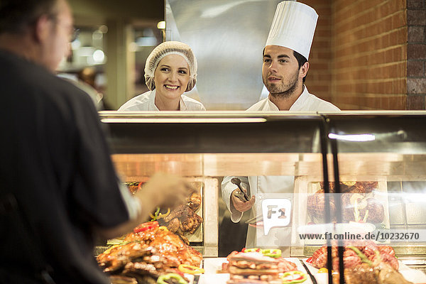 Chefkoch und Assistentin hilft Kunden bei der Speisenpräsentation