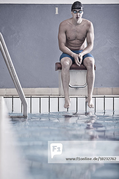 Schwimmer im Hallenbad auf dem Startblock sitzend