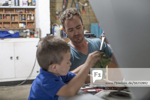 Son helping father in home garage working on car
