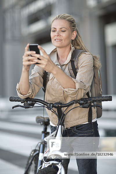 Blonde Frau auf dem Fahrrad mit dem Handy