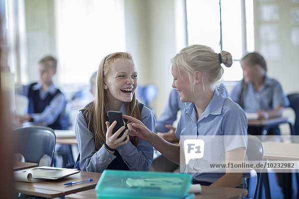 Zwei glückliche Schülerinnen im Klassenzimmer mit Handy