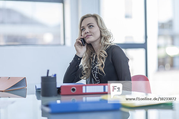 Portrait of blond woman telephoning with smartphone in an office