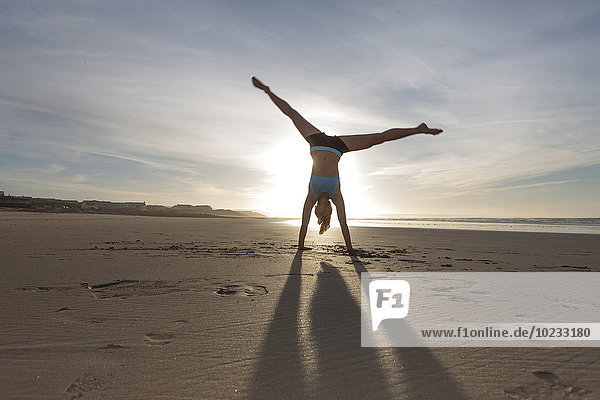 Südafrika  Kapstadt  Silhouette einer jungen Frau beim Handstand am Strand