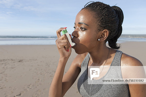 South Africa  Cape Town  young jogger using asthma inhaler on the beach