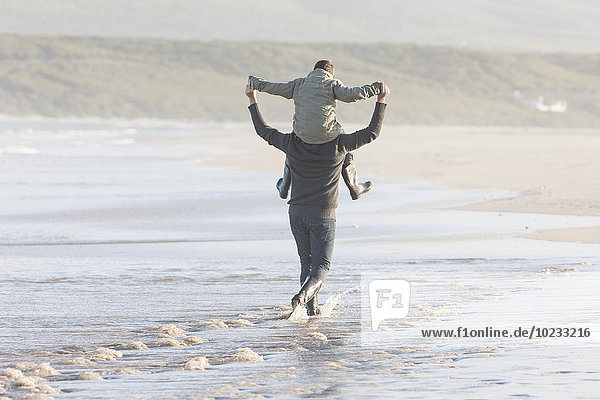 Südafrika  Kapstadt  Mann  der am Strand spazieren geht und seinen Sohn auf den Schultern trägt.