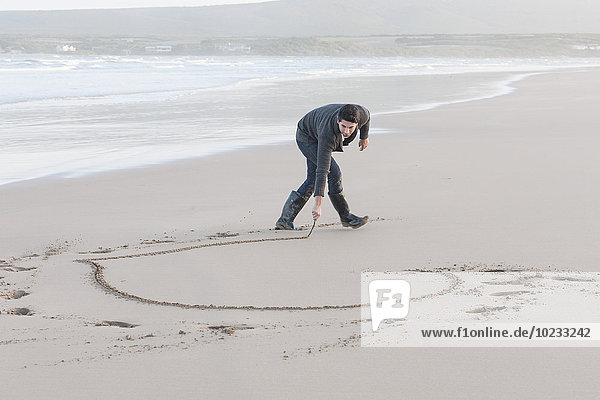 South Africa  Cape Town  man scratching heart in the sandy beach