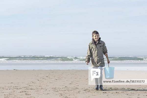 Südafrika  Witsand  Junge  der mit blauem Eimer am Strand spazieren geht