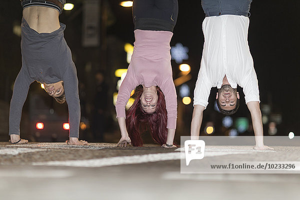 Three friends doing handstands on pavement at night