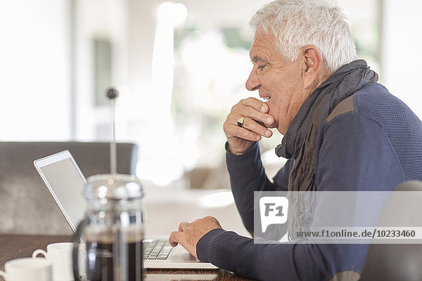 Senior Mann mit Laptop und Kaffeekanne zu Hause