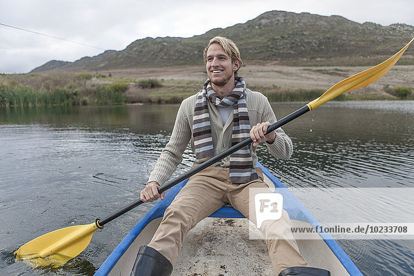 Portrait eines glücklichen jungen Mannes  der auf einem See paddelt.