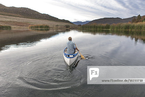 Rückansicht eines jungen Mannes beim Paddeln auf einem See
