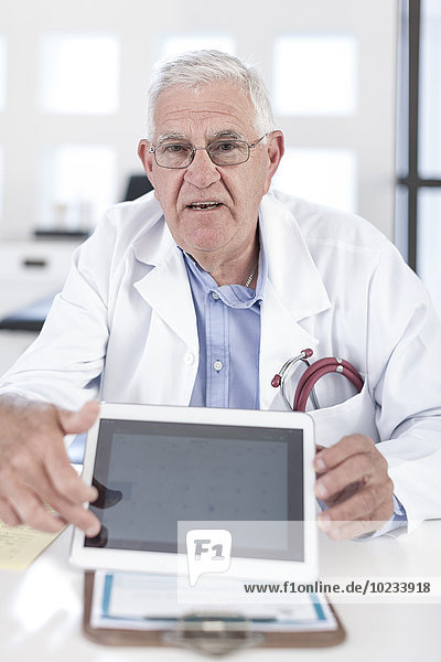 Serious senior doctor at desk showing digital tablet