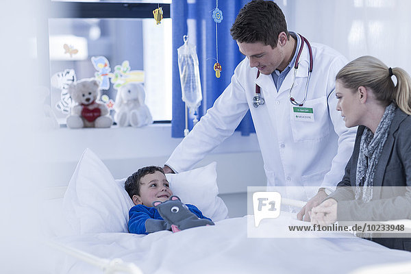 Mutter und Arzt besuchen kleinen Jungen im Krankenhausbett liegend