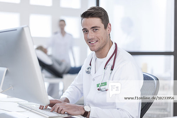 Portrait of smiling doctor sitting at desk working on computer