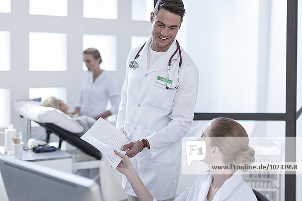 Lächelnder Arzt übergibt Dokument an Krankenschwester