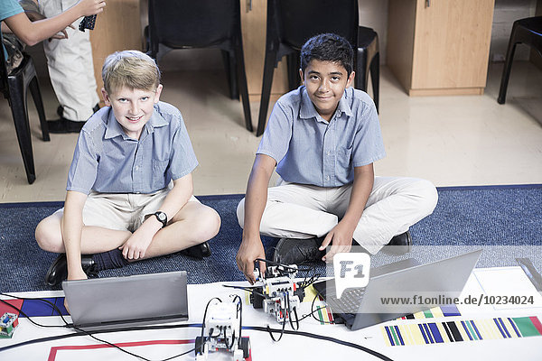 Two smiling schoolboys with laptops in robotics class