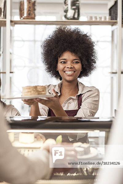 Young woman serving cake at cake counter in coffee shop