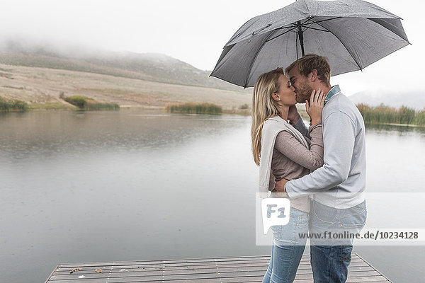 Küssendes Paar im Regen stehend mit Regenschirm