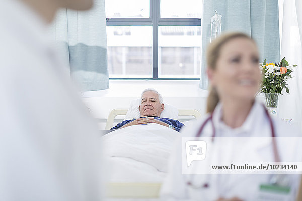 Senior man sleeping in a hospital bed while doctors discussing in the foreground
