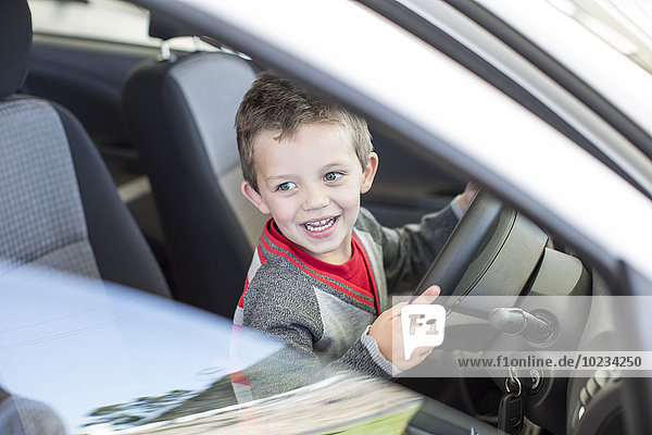 Happy boy at car dealer inside car steering