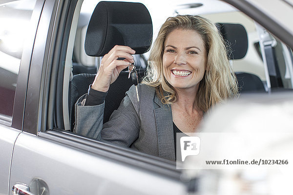 Porträt einer lächelnden Frau mit Schlüssel im neuen Auto