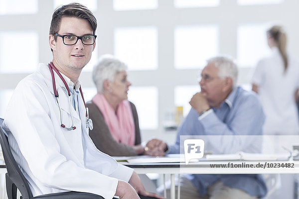 Doctor sitting at desk  worried senior couple in background