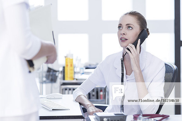 Krankenschwester am Schreibtisch am Telefon mit Blick auf den Arzt